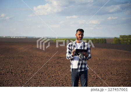 Digital tablet in hands. On cultivated agricultural field. Handsome Indian man 127457001