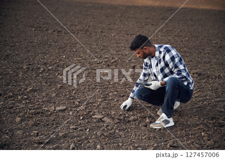 Cultivated agricultural field. Sitting, holding digital tablet. Handsome Indian man 127457006