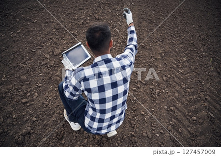 Cultivated agricultural field. Sitting, holding digital tablet. Handsome Indian man Cultivated agricultural field. Sitting, holding digital tablet. Handsome Indian man 127457009