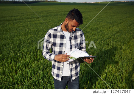 Reading the information from notepad. Handsome Indian man is on the agricultural field 127457047