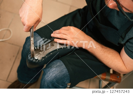 Working with nails on the shoe. Close up view of man that is sitting Working with nails on the shoe. Close up view of man that is sitting 127457243