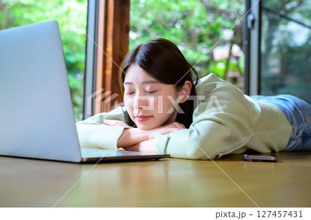 作業を終えてノートパソコンの前で腕を枕にして横になる女性が見せるリラックスの時間 127457431