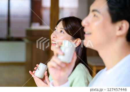 明るい和室で湯呑みを持った男女が顔を見合わせながら会話を楽しんでいる場面 127457446