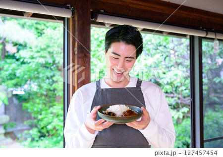 笑顔の男性が両手でハンバーグの皿を持ち、少しうつむいて見つめる仕草が印象的 127457454