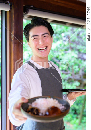 笑顔の男性がハンバーグを乗せた皿を斜めに構えて明るく元気な表情でポーズをとる 笑顔の男性がハンバーグを乗せた皿を斜めに構えて明るく元気な表情でポーズをとる 127457464