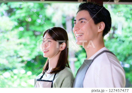 エプロン姿の男女が並んで窓の外を見つめながら明るく笑顔を見せる和風空間のワンシーン 127457477