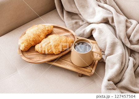 Coffee and croissants served on a wooden tray on a beige couch. Soft focus 127457504