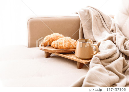 Coffee and croissants served on a wooden tray on a beige couch. Soft focus 127457506