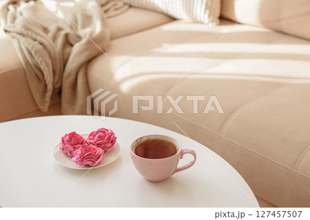 Pink flower marshmallows and tea on a coffee table with a cozy couch. Soft focus Pink flower marshmallows and tea on a coffee table with a cozy couch. Soft focus 127457507