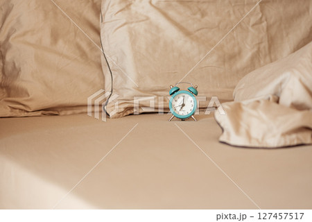 Alarm clock on an unmade bed in the morning light. Alarm clock on an unmade bed in the morning light. 127457517