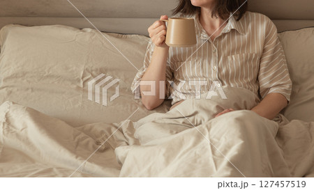 A woman enjoying coffee in a cozy bed. 127457519