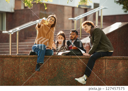 Woman is making selfie. Four young students in casual clothes are together outdoors 127457575