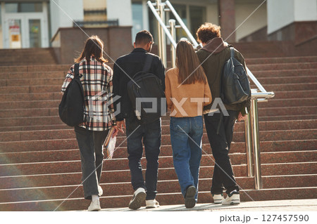 View from back, walking together. Four young students in casual clothes are outdoors View from back, walking together. Four young students in casual clothes are outdoors 127457590