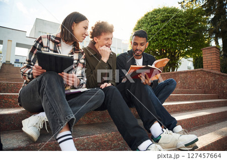 University building is behind. Young students in casual clothes are together outdoors University building is behind. Young students in casual clothes are together outdoors 127457664