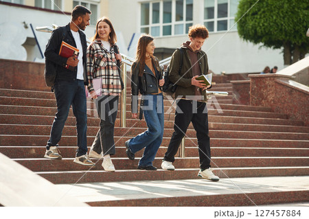 Going down the stairs. Four young students in casual clothes are together outdoors Going down the stairs. Four young students in casual clothes are together outdoors 127457884