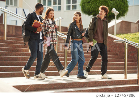 With education material in hands, notepads. Four young students in casual clothes are together outdoors With education material in hands, notepads. Four young students in casual clothes are together outdoors 127457886