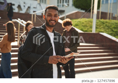 Indian man is standing in front of his friends. Four young students in casual clothes are together outdoors 127457896