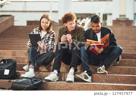 Students are sitting on the stairs. Young people in casual clothes are together outdoors 127457977