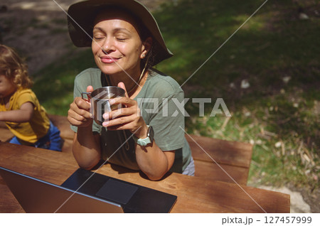 Woman Enjoying Online Work in Nature With a Refreshing Beverage Woman Enjoying Online Work in Nature With a Refreshing Beverage 127457999