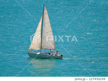 Sailing yacht race at sun light aerial. Yachting on serene seascape at open sea. Boat with big white spinnaker sail at ocean bay. Lonely ship cruise at water on summer sunny day. 127458249