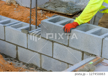 Construction worker constructing concrete block wall at building site during works daytime 127458863