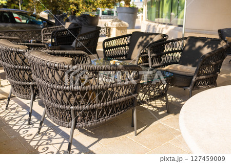 Outdoor wicker chairs with cushions in sunny cafe terrace. Modern outdoor seating, cozy atmosphere, and leisure lifestyle. Outdoor wicker chairs with cushions in sunny cafe terrace. Modern outdoor seating, cozy atmosphere, and leisure lifestyle. 127459009