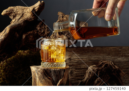 Whiskey is poured from a bottle into a glass. Whiskey is poured from a bottle into a glass. 127459140
