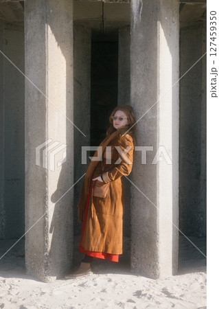 woman in a brown coat stands in front of a pillar.  127459350