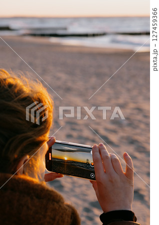 woman takes pictures of the ocean on her mobile phone.  127459366