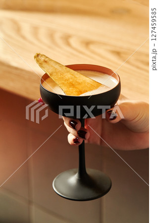 Woman holding a coupe glass with a cocktail and a garnish 127459585