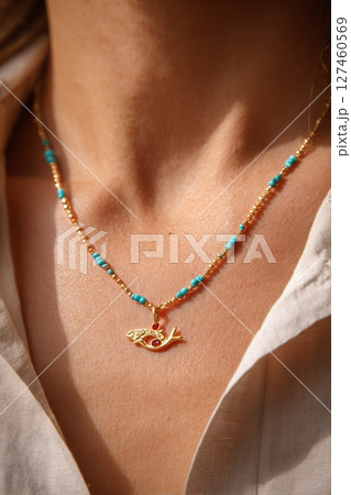Beautiful Gold and Turquoise Necklace Adorned With a Fish Pendant Against a Neutral Background 127460569