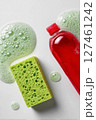 Bright Green Sponge and Red Soap Bottle With Bubbles on a White Surface During a Cleaning Session 127461242