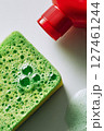 Bright Green Sponge and Red Soap Bottle With Bubbles on a White Surface During a Cleaning Session. 127461244