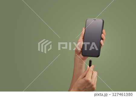 female hand plugging charger cord into smartphone to charge battery on green background, copy space female hand plugging charger cord into smartphone to charge battery on green background, copy space 127461380