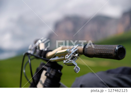 Close-up of mountain bike handlebars against out-of-focus mountain landscape. Mountain downhill cycling Close-up of mountain bike handlebars against out-of-focus mountain landscape. Mountain downhill cycling 127462125