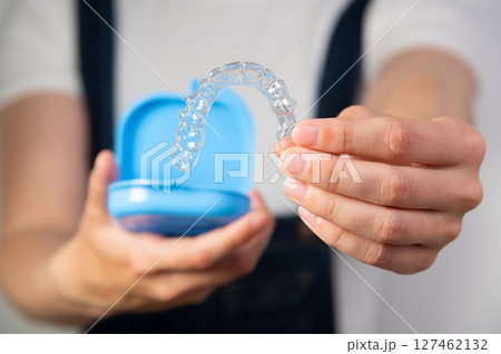 Hands of a young Caucasian woman holding transparent dental aligners and a case for storing them. Plastic braces with space copy Hands of a young Caucasian woman holding transparent dental aligners and a case for storing them. Plastic braces with space copy 127462132