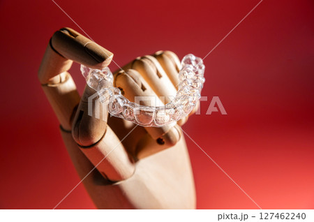 Teeth alignment trays on pink background in wooden fake hand. Modern teeth alignment, technology, billboard or website advertising layout 127462240