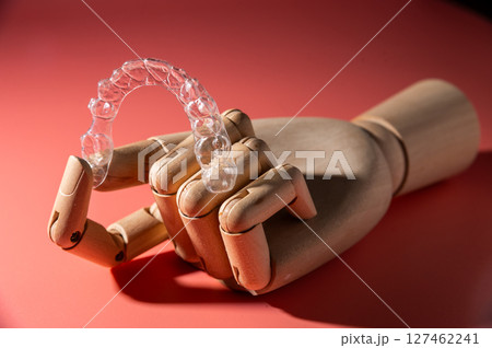 Teeth alignment trays on pink background in wooden fake hand. Modern teeth alignment, technology, billboard or website advertising layout 127462241