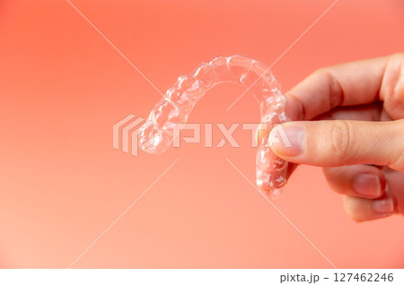 Hand hold invisible aligners plastic braces dentistry retainers to straighten teeth temporary removable straightener with plastic dentures on light peach background 127462246