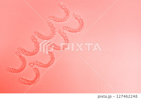 Invisible teeth retainers lie on a bright pink background. Close-up of a modern way to straighten teeth 127462248
