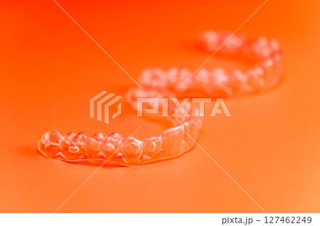 Invisible teeth retainers lie on a bright orange background. Close-up of a modern way to straighten teeth 127462249