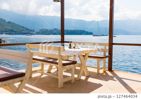 Outdoor cafe or restaurant with sea view and empty chairs. Coastal relaxation, summer tourism, and beachfront dining in the Mediterranean region. 127464034