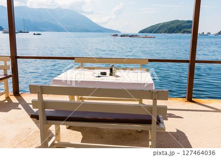 Outdoor cafe or restaurant with sea view and empty chairs. Coastal relaxation, summer tourism, and beachfront dining in the Mediterranean region. 127464036