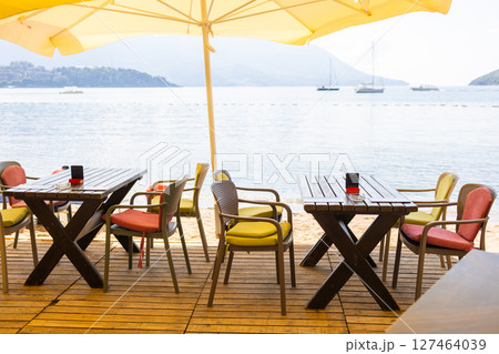 Outdoor cafe or restaurant with sea view and empty chairs. Coastal relaxation, summer tourism, and beachfront dining in the Mediterranean region. 127464039