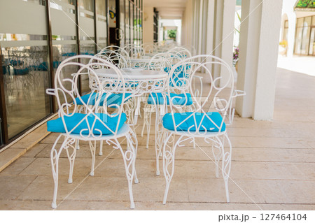 White patio chairs with blue cushions in sunny veranda. Outdoor elegance, Mediterranean leisure, and summer hospitality design. 127464104