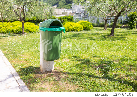 Green park trash bin in spring sunlight. Clean environment, urban maintenance, and public cleanliness awareness. 127464105