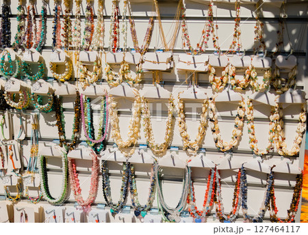 Colorful necklaces made of shells and gemstones on market display. Beach fashion, handmade souvenirs, and traditional crafts for tourists in coastal destinations. Colorful necklaces made of shells and gemstones on market display. Beach fashion, handmade souvenirs, and traditional crafts for tourists in coastal destinations. 127464117