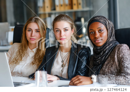 Diverse group of women in professional attire collaborating in modern office environment 127464124