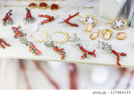 Red coral jewelry display in artisan shop. Handcrafted accessories, marine motifs, and Mediterranean design influence local fashion and cultural aesthetics. Red coral jewelry display in artisan shop. Handcrafted accessories, marine motifs, and Mediterranean design influence local fashion and cultural aesthetics. 127464135