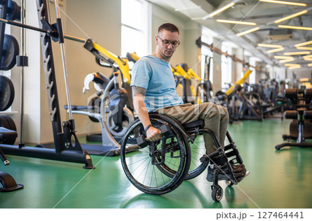 Post accident athlete. Determined disabled man in wheelchair training arms and shoulders with weight Post accident athlete. Determined disabled man in wheelchair training arms and shoulders with weight 127464441